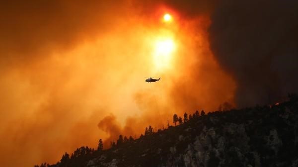 A helicopter flies over a wildfire.