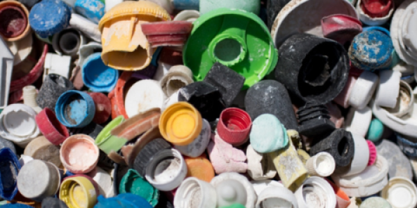 Multiple different colored caps and bottles gathered into a sizable pile with sand visible on the macroplastic debris.