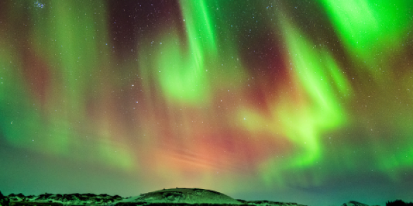 Green and red colors from an aurora over a mountainous landscape and large body of water.