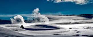 Picture of a snowy Yellowstone National Park underneath a blue, cloudy sky.