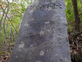 Large grey stone stands in the woods with Japanese inscriptions. 