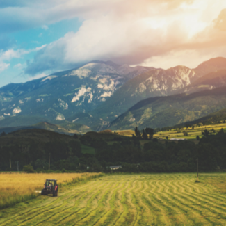 Tractor in crop field with mountains with in background and white clouds overhead