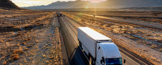 Semi driving on a road through the desert with mountains in the background