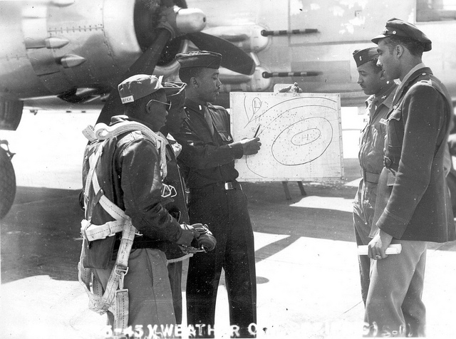 A black and white photo of five Tuskegee airmen studying a meteorological chart. 