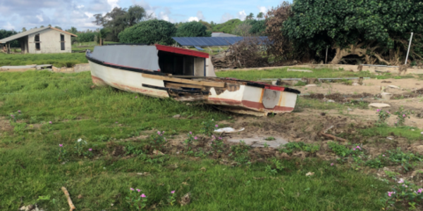A damaged boat washed up into the middle of a field in front of a hut.