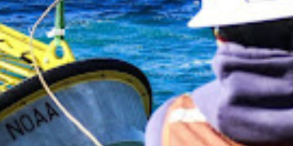 Technician wearing safety gear deploys yellow buoy into blue-green ocean.