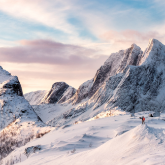 Panoramic image of snow covered mountains with a person far away in the background. 