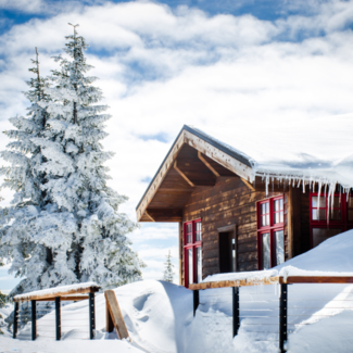 Snow-covered wooden cabin with snow drifts piled high on the porch.
