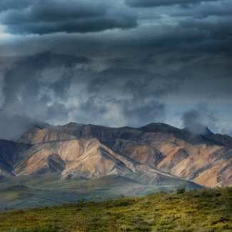 Dark storm clouds over layered mountains, and green grass in the forefront.