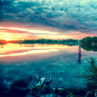 An American flag on a pole in front of a lake at sundown.