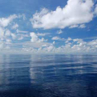 Fair weather cumulus clouds reflecting off of a glassy smooth ocean.
