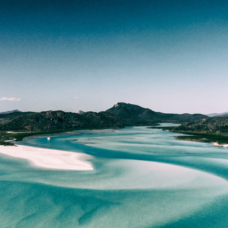  Queensland Beaches in Australia with dark blue sandy water and mountains rising in the distance.