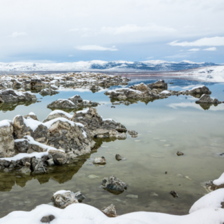A lake with boulders strewn throughout the water with snow-capped mountains looming in the background.