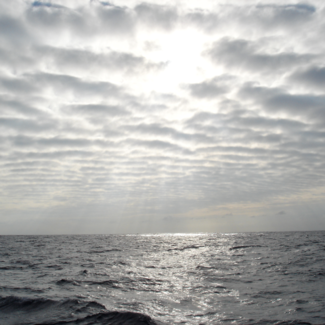 Sunlight filters through clouds to shine on open ocean