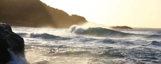 Waves crashing on beach cliffs during sunrise. 
