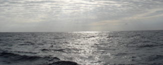 Sunlight filters through clouds to shine on open ocean